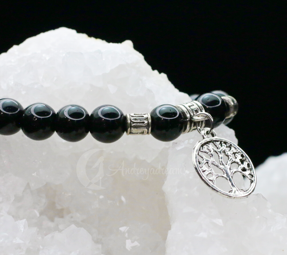 Pulseira Ónix com Árvore da Vida Pulseira preta com pendente prateado de árvore sobre superfície branca cristalina