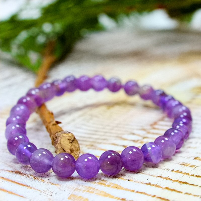 Pulseira Ametista Pulseira de contas roxas de ametista sobre madeira com ramo verde ao fundo