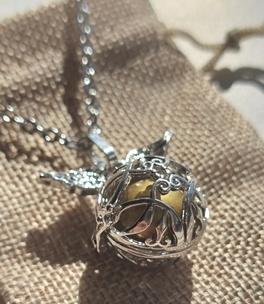 Chamador de Anjos com Asas Colar prateado com pingente esférico decorativo sobre tecido bege