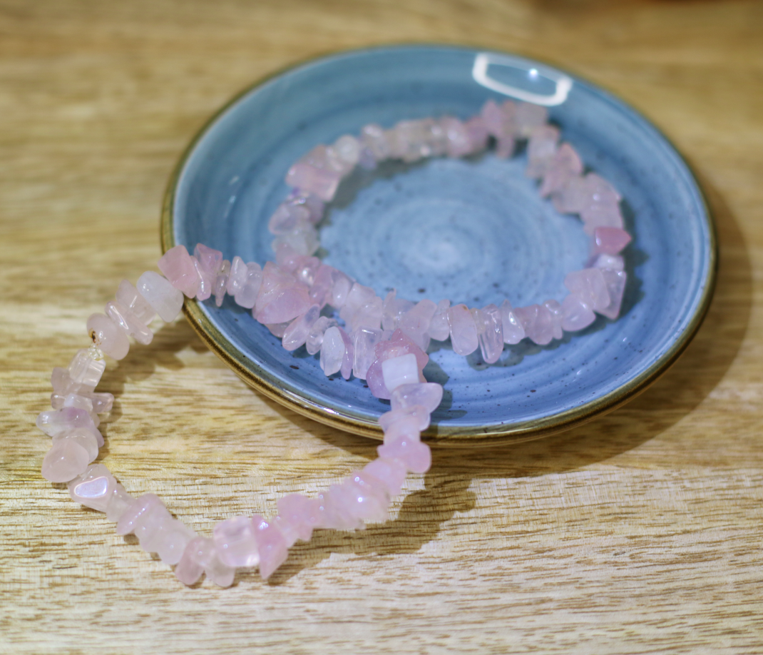 Pulseira Quartzo Rosa Chips Duas pulseiras com pedras cor-de-rosa num prato azul sobre mesa de madeira