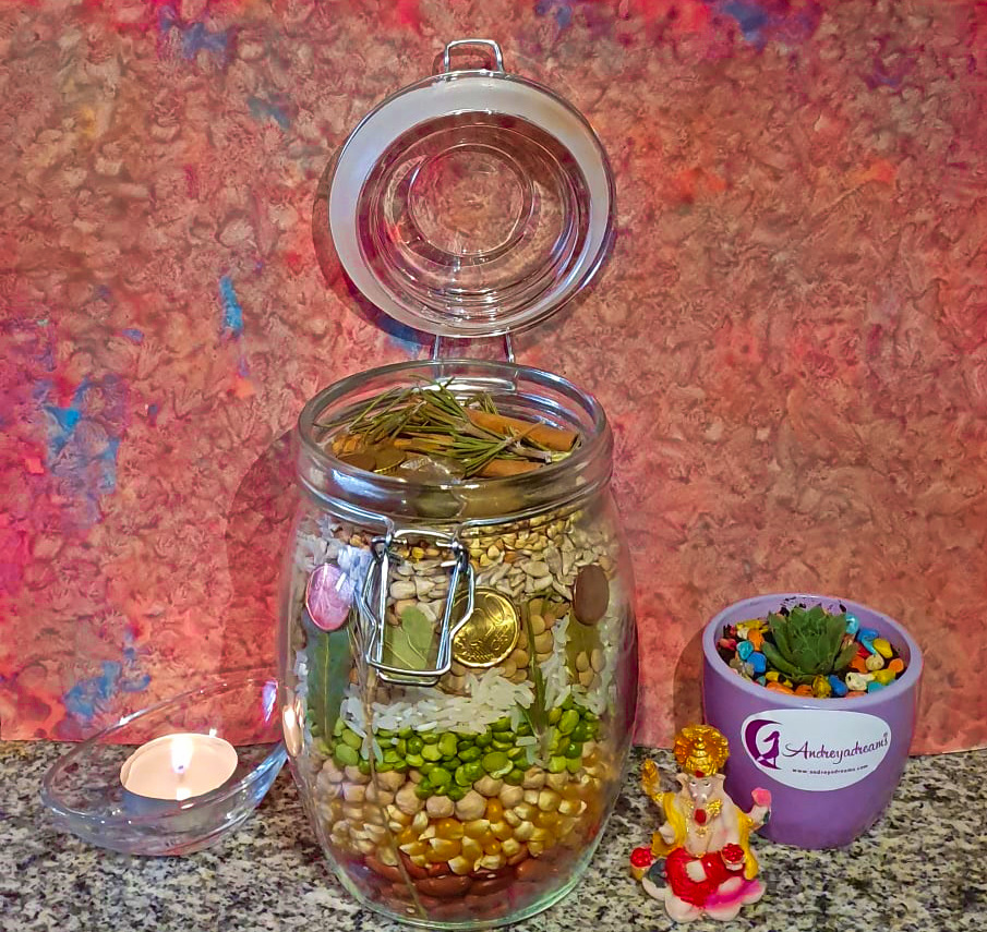 Frasco de vidro com grãos e folhas secas, vaso lilás com planta suculenta e vela em superfície de pedra