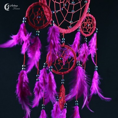 Filtro dos sonhos vermelho com penas cor-de-rosa e contas pretas num fundo preto.