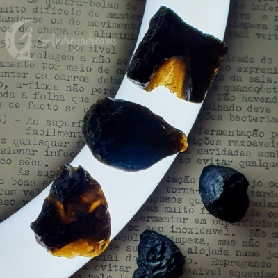 Fragmentos pretos e âmbar sobre superfície branca curva com texto impresso em papel ao fundo