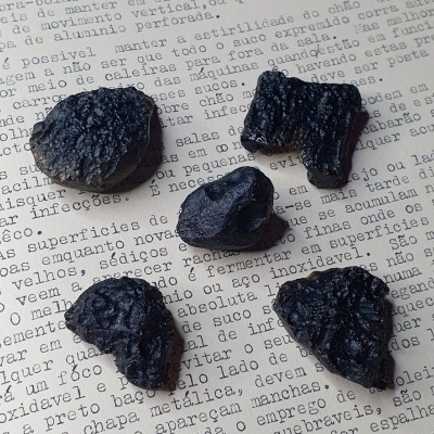Cinco pedaços de carvão negro sobre papel com texto em português