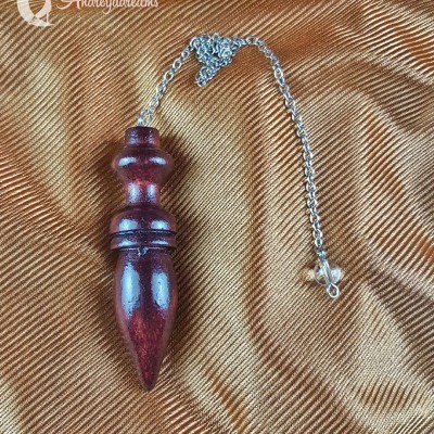 Pêndulo em madeira escura polida com corrente de metal prateado sobre tecido dourado