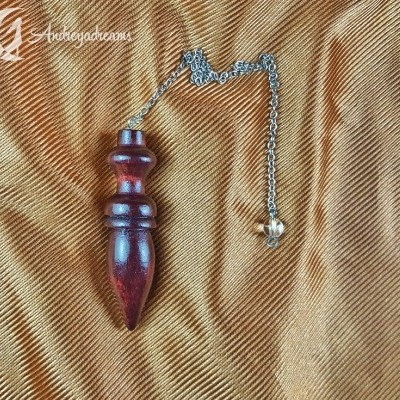 Pêndulo de madeira escura com corrente metálica sobre tecido castanho