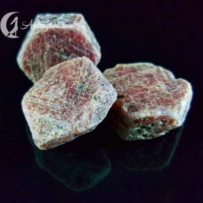 Três pedras minerais avermelhadas com veios brancos sobre superfície preta refletora