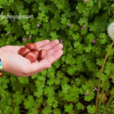 Mão com pulseira segurando corações de madeira sobre fundo verde com flores