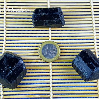 Três minerais pretos ao redor de uma moeda de 1 euro sobre uma esteira de bambu