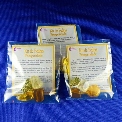 Três kits de pedras para prosperidade em sacos plásticos com etiquetas amarelas sobre fundo azul