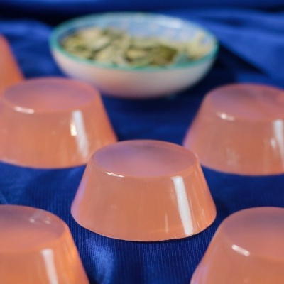 Gelatinas cor de rosa translúcidas sobre tecido azul com tigela de sementes ao fundo