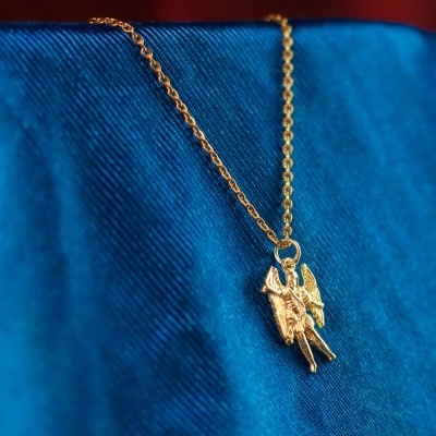 Colar dourado com pendente de anjo sobre tecido azul