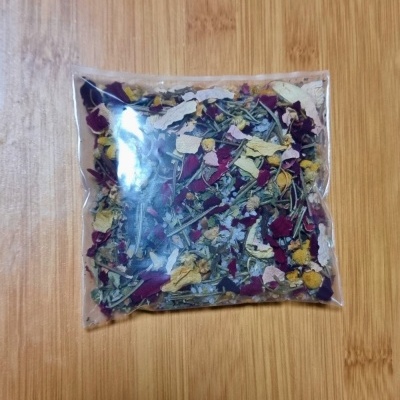 Pacote de mistura de flores secas e folhas coloridas num saco plástico sobre madeira clara