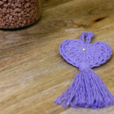 Chaveiro em forma de coração roxo tricotado com pérola e franja sobre madeira