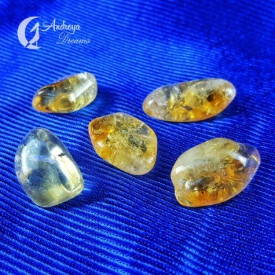 Cinco pedras polidas de âmbar amarelo e laranja sobre tecido azul com logo Andeya Dreams