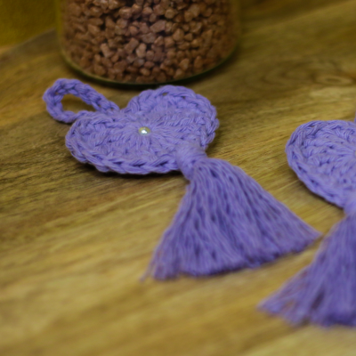 Corações de tricô lilás com pérola e tassel, sobre madeira clara