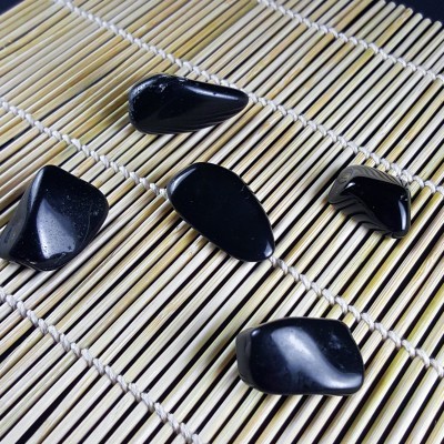 Cinco pedras pretas polidas sobre tapete de palha com padrão de linhas.