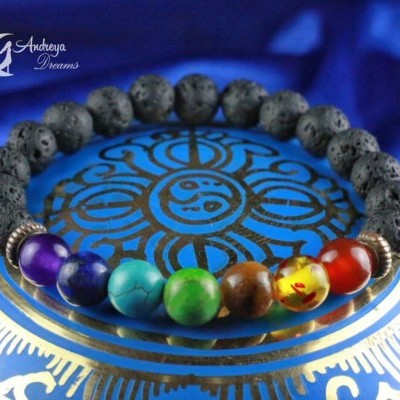 Pulseira com contas coloridas e de lava vulcânica sobre superfície azul com padrão dourado