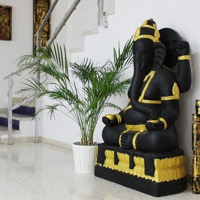 Estátua preta e dourada de Ganesha junto a planta e bastões decorativos num ambiente interior