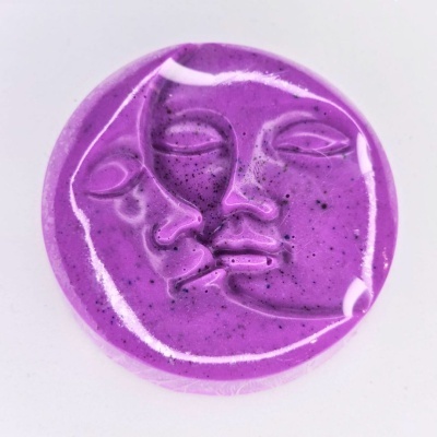 Objeto redondo roxo com relevo de dois rostos sobre fundo branco