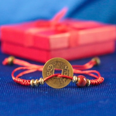 Pulseira vermelha com moeda chinesa e contas metálicas, caixa vermelha ao fundo