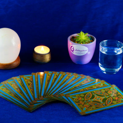 Cartas de tarô em leque, vela acesa, bola de cristal, planta suculenta em vaso e copo de água sobre tecido azul