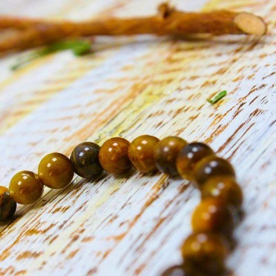 Colar ou pulseira com contas castanho dourado brilhantes sobre madeira clara texturizada e pequeno ramo seco