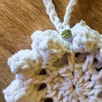 Peça em croché branca com etiqueta metálica 