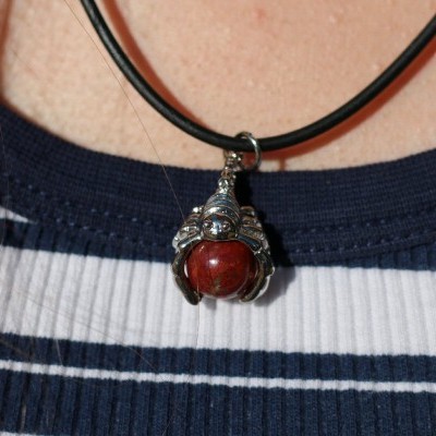 Colar com pendente prateado e esfera vermelha em cordão preto sobre t-shirt riscada azul e branco