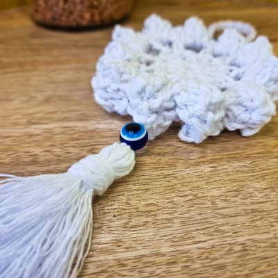 Chaveiro macramé branco com conta azul olho turco sobre madeira clara.