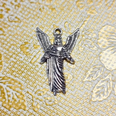 Pingente de anjo prateado sobre tecido branco com padrão dourado