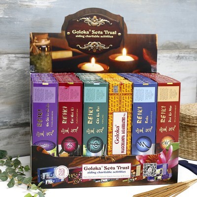 Expositor de incensos Goloka Seva Trust com caixas coloridas e velas acesas ao fundo