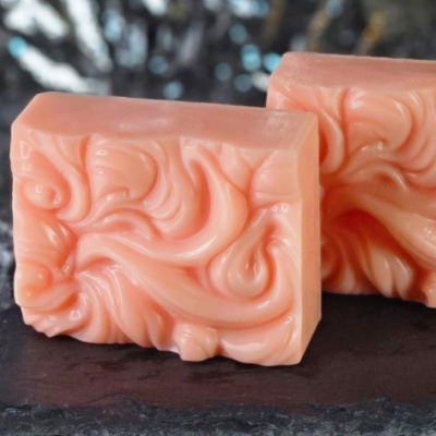 Dois sabonetes laranja claro com textura ondulada sobre pedra escura