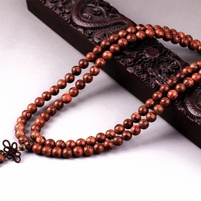 Colar de contas de madeira castanha com pendente sobre base de madeira escura entalhada