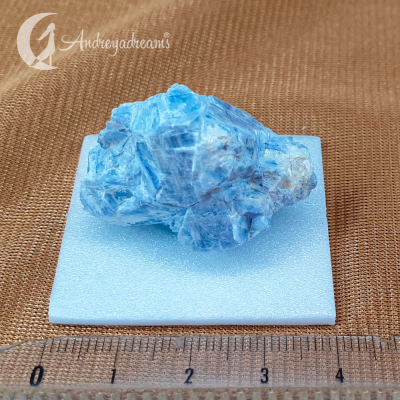 Roca mineral azul sobre base branca com régua em fundo castanho