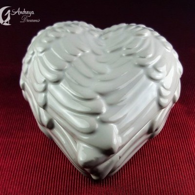 Caixa de cerâmica branca em forma de coração com textura de penas sobre tecido vermelho