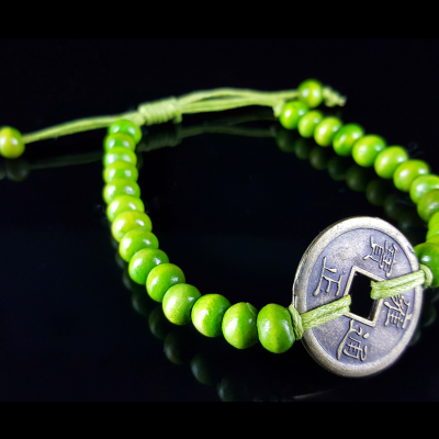 Pulseira com contas verdes e pendente metálico com inscrições asiáticas