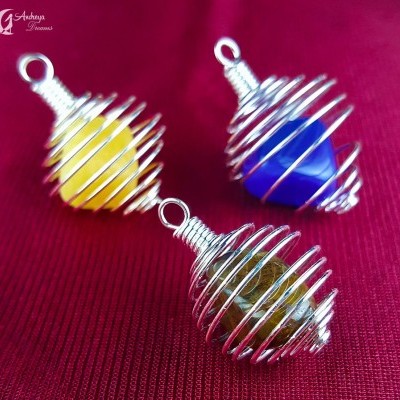 Três pingentes de pedra com espiral metálica sobre tecido vermelho