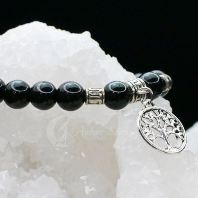 Pulseira preta com pendente prateado de árvore sobre superfície branca cristalina