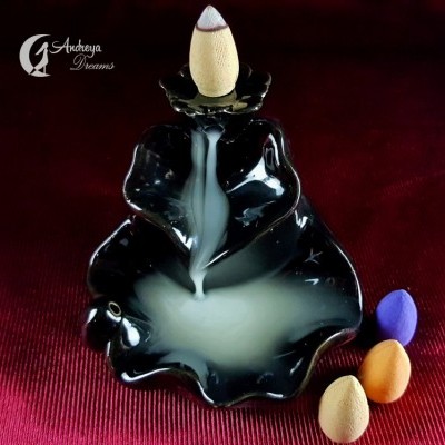 Incensário preto em forma de folha com cones de incenso coloridos ao lado e fumaça a descer