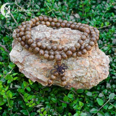 Colar de contas marrons com pingente sobre pedra e folhagem verde