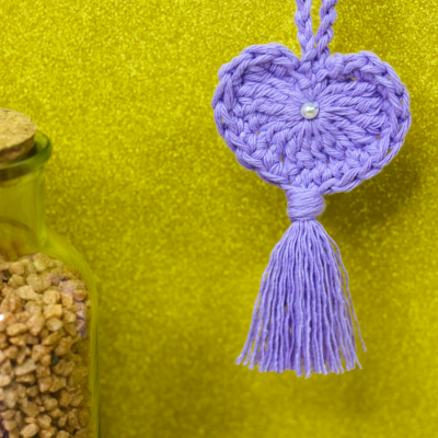 Coração lilás de croché com pérola e franja pendurado ao lado de garrafa com pedras