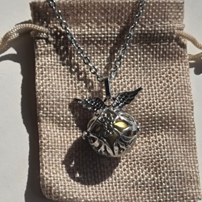 Colar prateado com esfera decorada e asas sobre saco de tecido bege