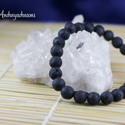 Pulseira de contas pretas em pedra vulcânica sobre cristal branco e tapete de bambu.