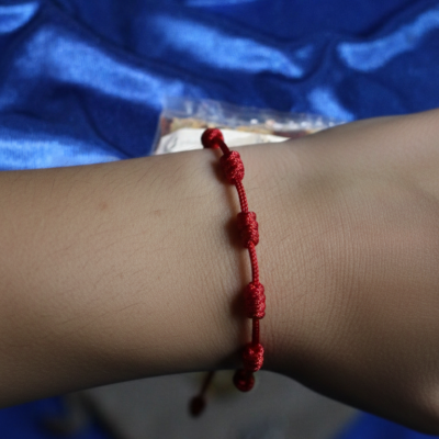 Pulseira vermelha com nós decorativos no pulso sobre tecido azul