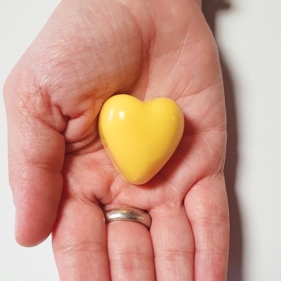 Mão segurando um coração amarelo brilhante