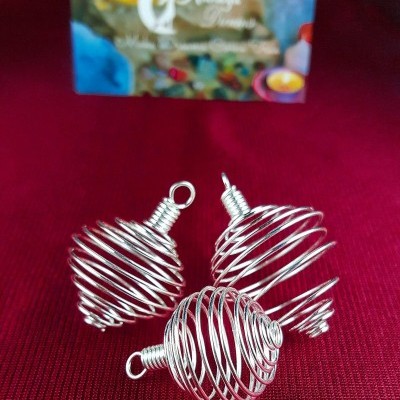 Três gaiolas espiraladas em arame prateado sobre tecido vermelho com cartão colorido em fundo