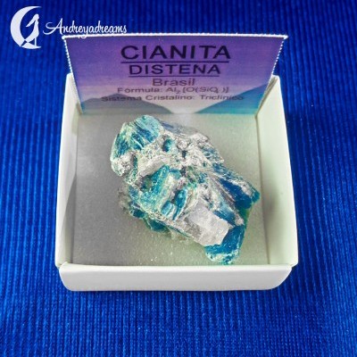 Cianita azul clara em caixa branca com cartão informativo e fundo azul.