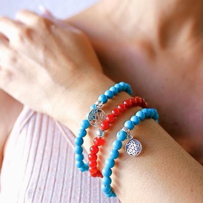 Três pulseiras de contas azuis e vermelhas com pingentes prateados no pulso