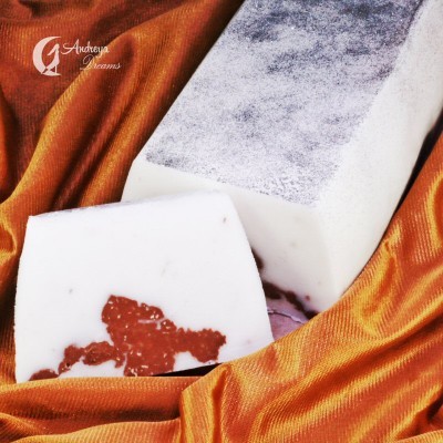 Barra de sabão branca com manchas castanhas e superfície cinzenta sobre tecido laranja